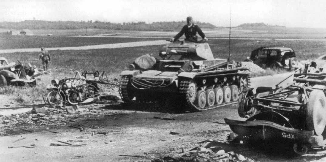 A Panzer II moving past wrecked vehicles in open country after the breakout.